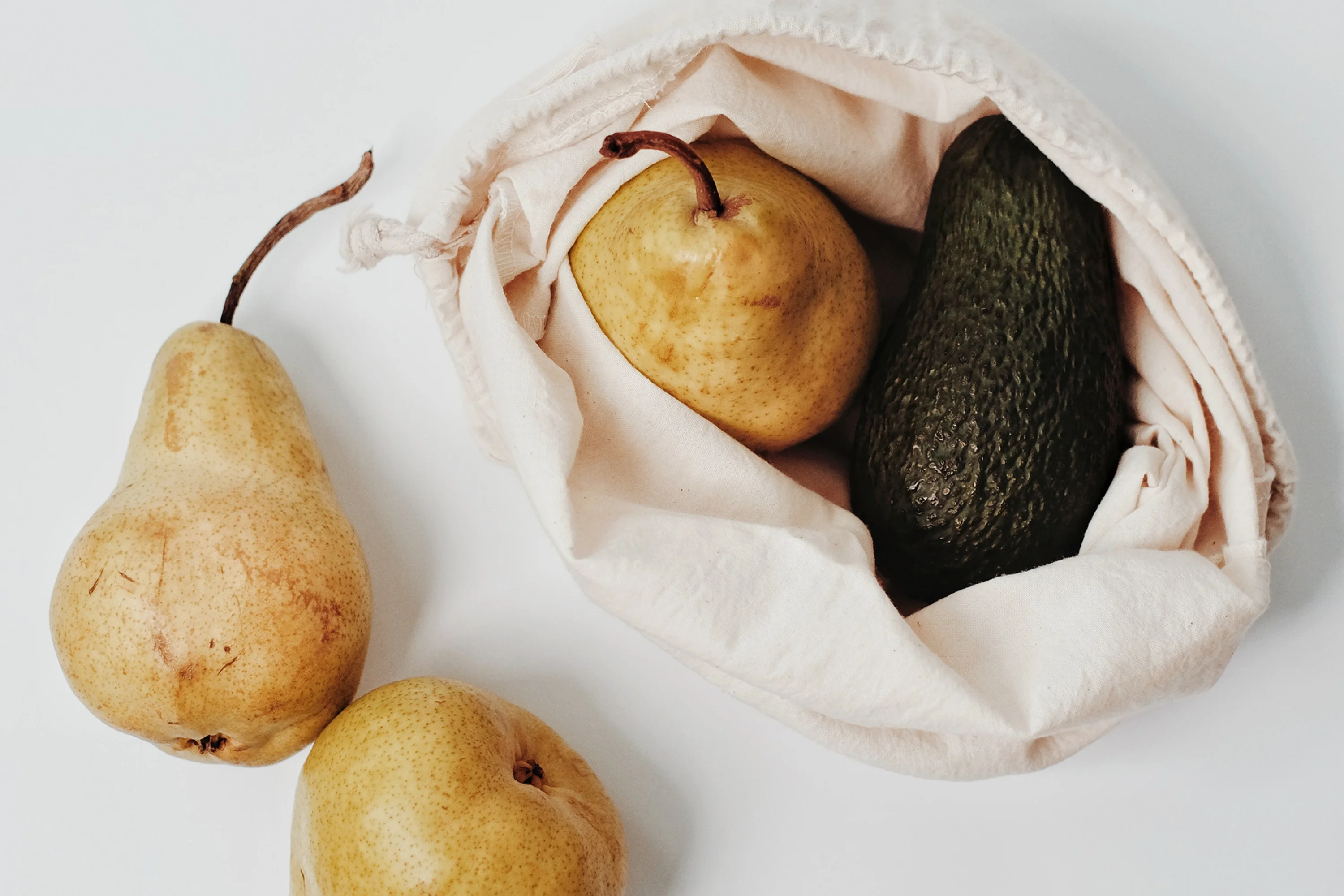 three pears and one avocado in a canvas bag